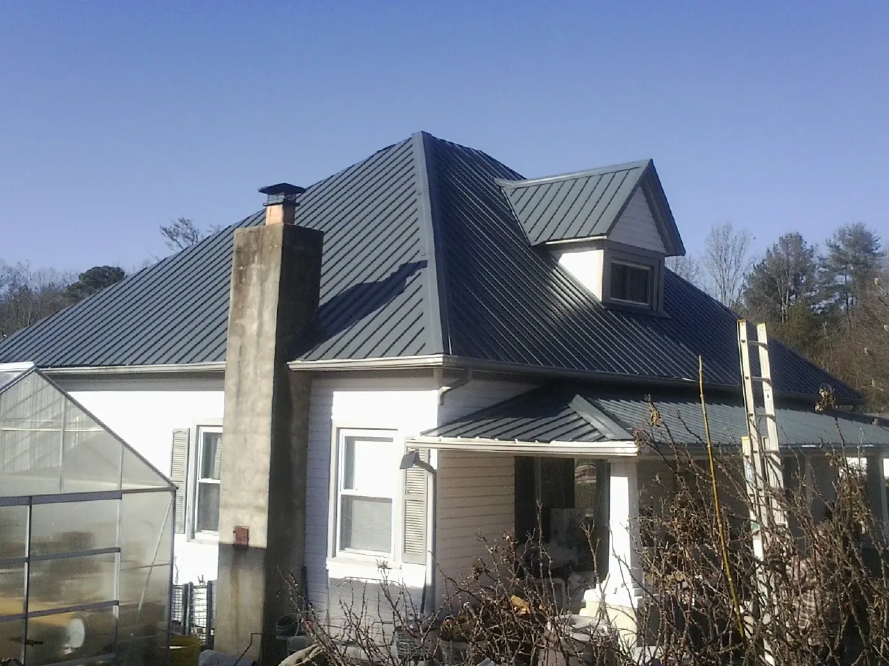 Dark blue standing seam metal roof on a white farmhouse with dormer — Slate & Tile Roof Repair by Roofing Brothers in Caret