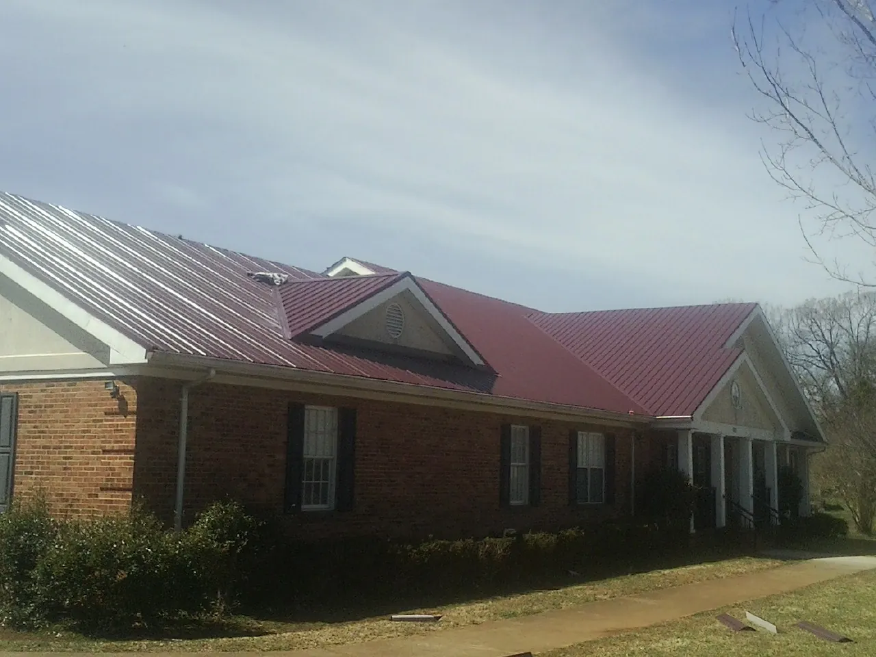 Red metal roof with gabled entries on a long brick building, from a Hail Damage Roof Repair job in Caret