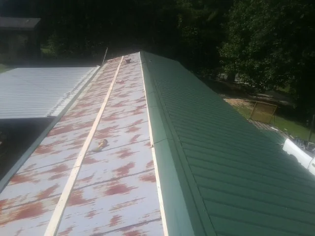 Old rusted panels beside newly installed green metal roofing — Wind Damage Roof Repair by Roofing Brothers in Caret