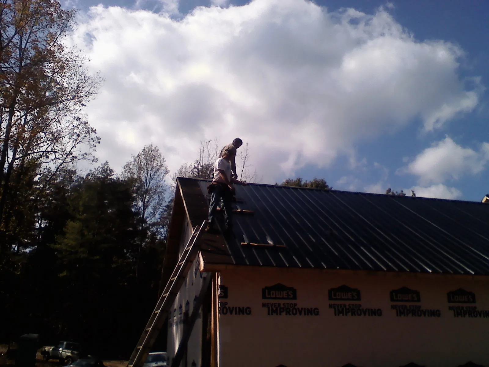 Roofer fastening dark metal panels high against a cloudy sky, from a Roof Inspection job in Caret