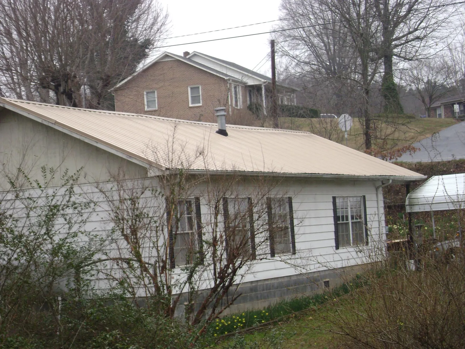 Tan metal roof on a white sided house set into a hillside — Commercial Roofing by Roofing Brothers in Caret